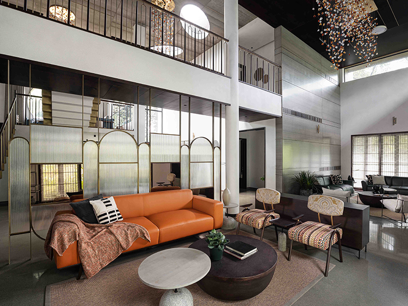 The double-height living room features a statement chandelier with cascading leaves that contribute to the play of light and shadow. (Image Credits: Turtle Arts)