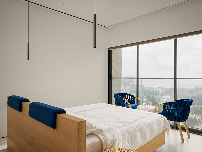 With natural light filtering in through the French windows, the bedroom with its wooden accents and Knit Armchair by Kenneth Cobonpue basks in the golden light. (Image Credits: Isha Shah)