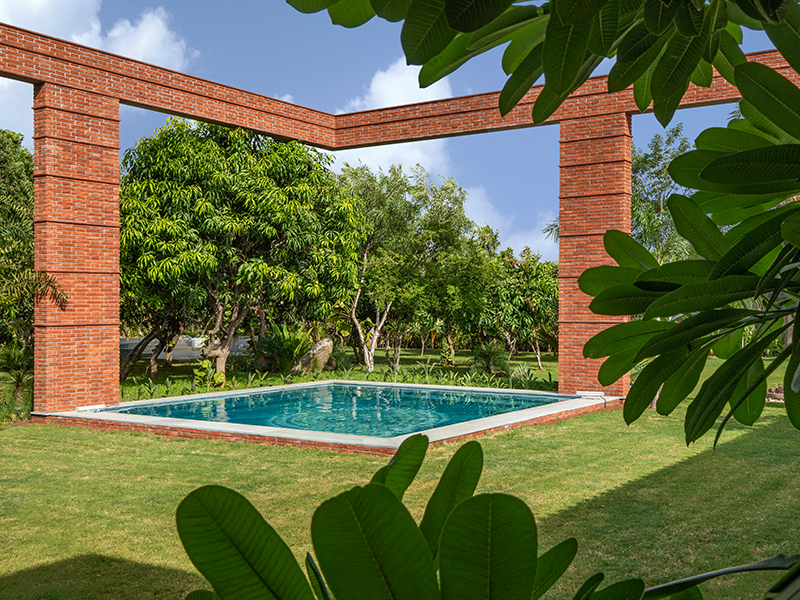 Tall frames of exposed brick serve to demarcate and set the boundaries for the swimming pool. (Image Credit: Tejas Shah)