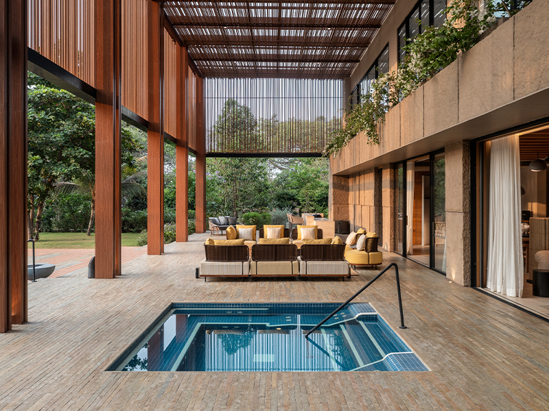 The double-height veranda is the central core of the home, straddling the indoors and outdoors with an interplay of light and shadow. It features large and small seating areas with furniture by Lavish Line, a bar, and a jacuzzi. (Image Credits: PHX India)