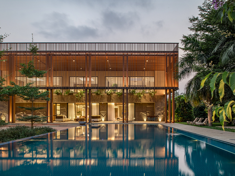 Wooden fins encircle the entire top floor, filtering the heat and light that pass through and regulating the indoor climate, while ensuring uninterrupted views of the lush surroundings. (Image Credits: PHX India)