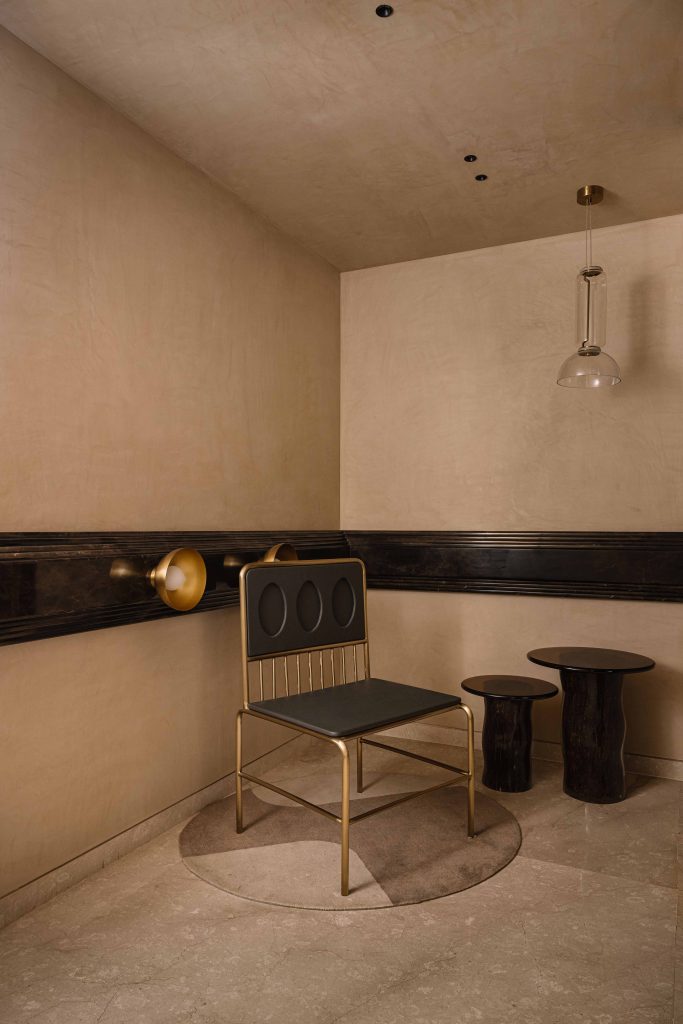 Brass and timber lend a lived-in glow to this space, while a chair and table from Poshway sit gracefully beneath a pendant from Poshway that casts a subtle sheen on the beige walls, finished in elegant tones by Bombay Paints. (Image Credits: Ishita Sitwala)