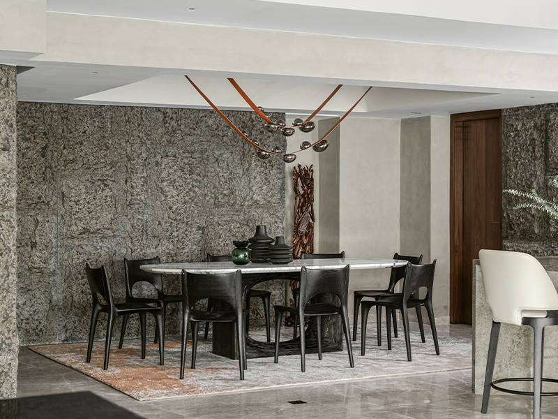 In the dining area, textured basalt walls become the perfect backdrop to a striking ALC Studio pendant inspired by droplets of dew. (Image Credits: Nayan Soni)