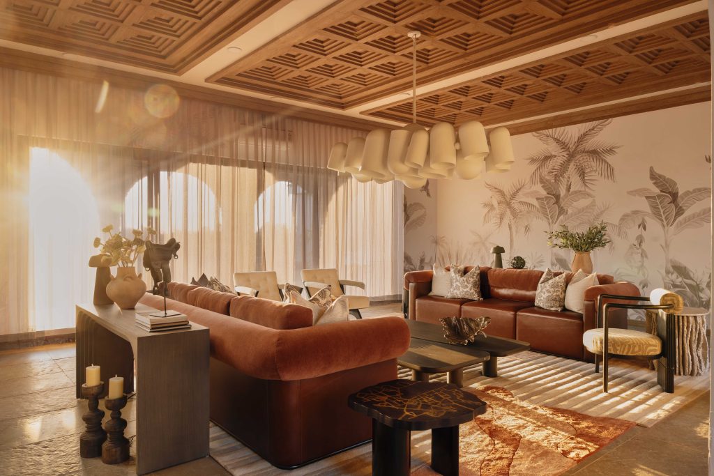 The living room commands attention with a dramatic cluster of Guccha light—lingam-inspired forms suspended mid-air by Ashiesh Shah Studio. Plush sofas from Ziba Homes and accent chairs from The House of Things add comfort and character, while tropical palms and beach-inspired wallpaper by Artisan Furnishings tie the entire space together with a sense of laid-back elegance. (Image Credits: The Matter Studio)  