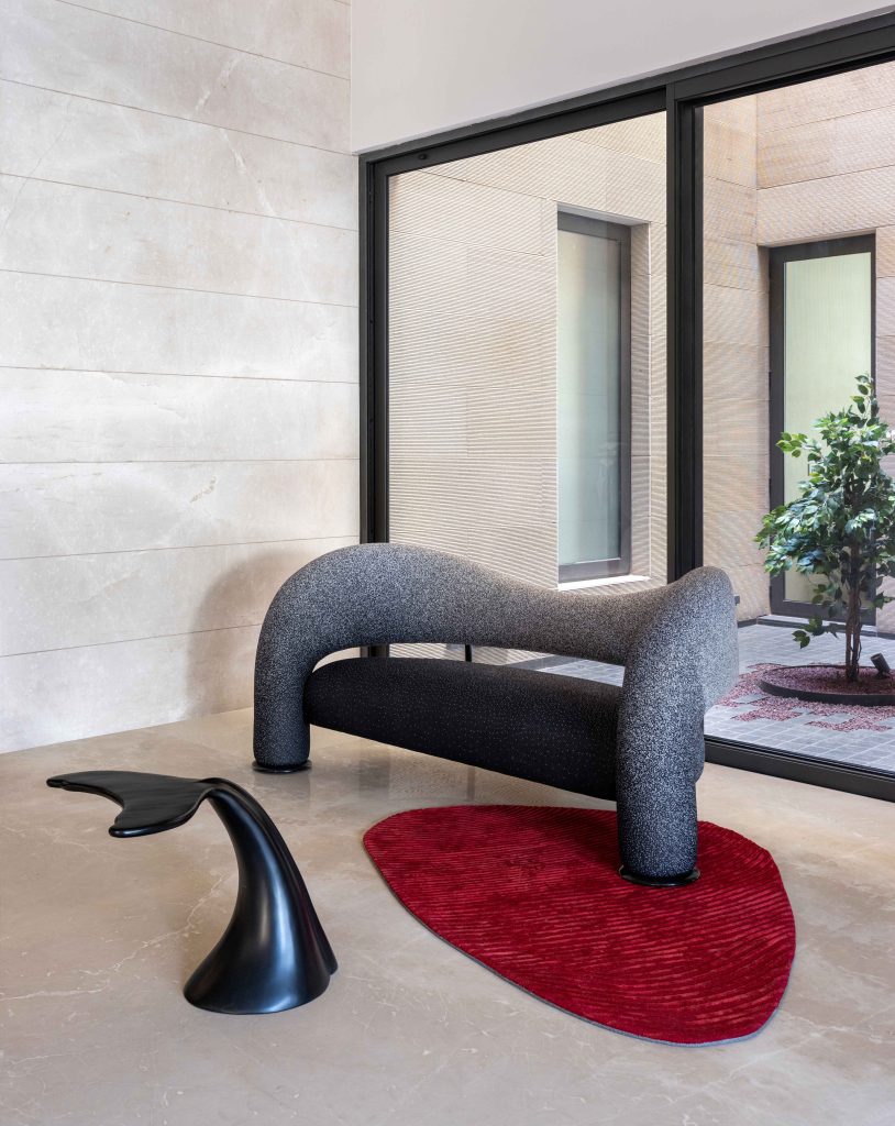 The foyer sets the tone for the home’s robust interplay of form, materiality and colour. A fluid black accent table by Nama Home, custom curvilinear monochrome seating, and a crimson rug custom-made from Prince Home Furnishing reinforce the tension between structure and spontaneity. (Image Credits: Purnesh Dev Nikhanj)