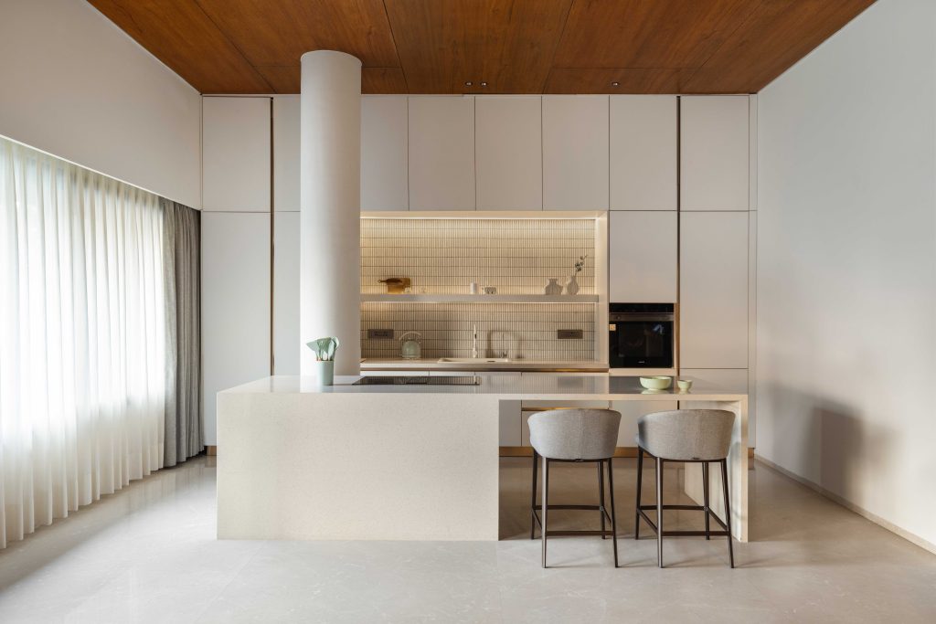 The kitchen by Atul Interiors marries sleek cabinetry with a neutral palette, clean lines, integrated appliances and warm lighting. KitKat mosaic tiles from La Casa Decor add subtle texture, while quartz countertops from KalingaStone enrich the overall materiality. (Image Credits: Purnesh Dev Nikhanj)