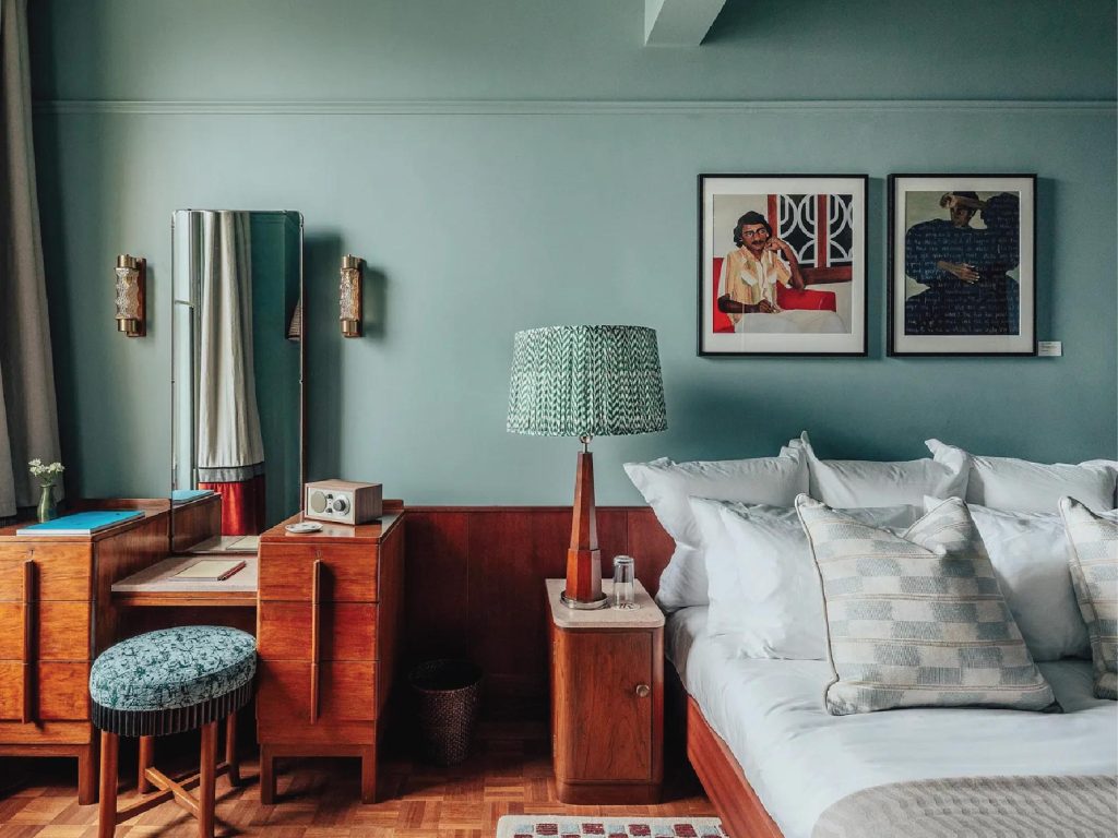 Art Deco light fixtures, a mid-century modern dressing table, vintage writing pads, a retro radio, and a bold geometric rug from Jaipur Rugs create an effortlessly elegant mood in the master bedroom. Image Credit: (Permit Room Lodgings)