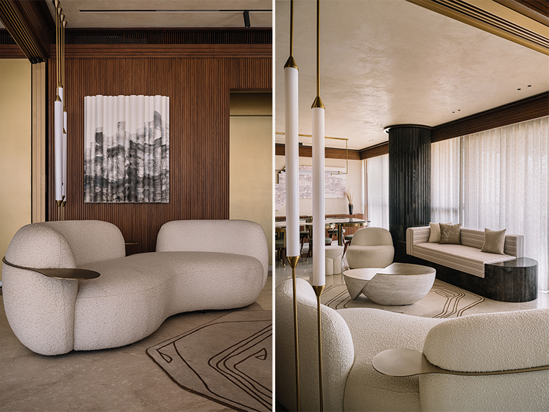 Left: The bouclé couch from Poshway, perched atop a rug from Atelier Textile Epic, sits in perfect contrast against the wooden backdrop, while a stone artwork from Poshway tells tales of exquisite craftsmanship. Right: Colossal French windows drench the sculptural partition, curated art, and cosy stone couch from Poshway in natural light, while spilling onto a balcony that opens to sweeping city views. (Image Credits: Ishita Sitwala)