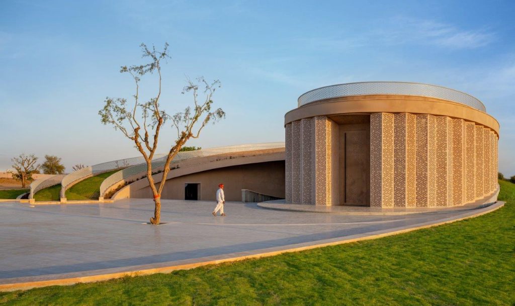 The façade, sculpted in sandstone with intricate jali screens and wrapped in an earth berm while offering climate-responsive shelter. (Image Credits: Vinay Panjwani)