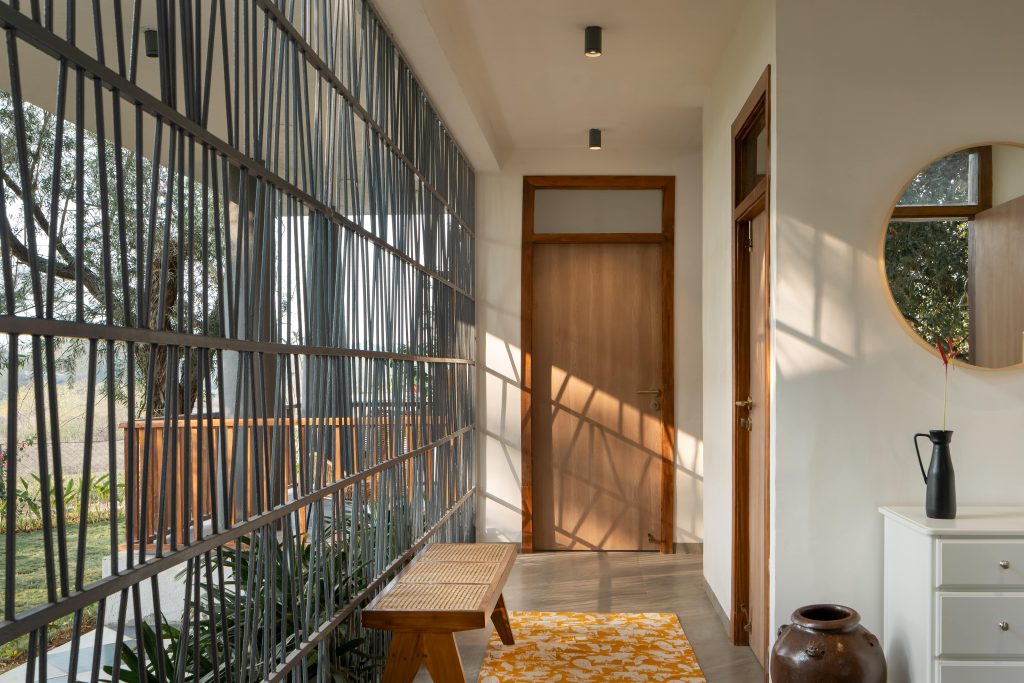 The mullioned screen along the breezeway orchestrates an interplay of light and shadow on the wood wicker bench from Freedom Tree and the rug from Saphed Home, while the vases are from Ware Innovations. (Image Credits: Ekansh Goel)
