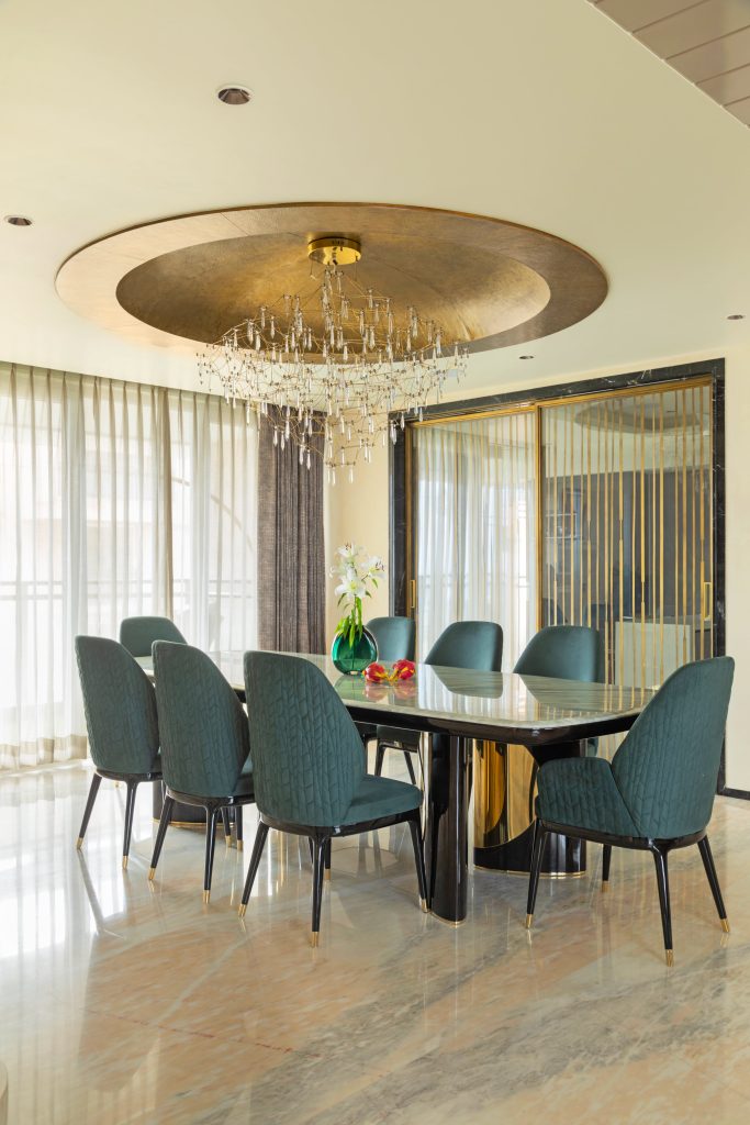 The dining area features a custom-made solid wood table, set against Michael Angelo marble flooring. Overhead, a brass dome, made with a single sheet of brass, and dangling pendants from Ledos add a warm, focused glow that ties in with the home’s understated material palette. (Image Credits: Gitesh Gupta, Studio Bluora)