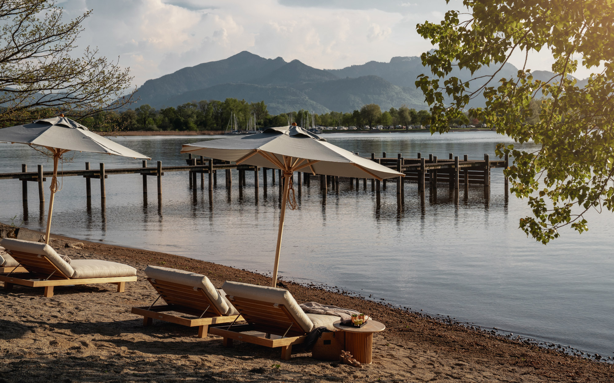 The outdoor Chiemgauhof Beach Club is outfitted with elegant, luxuriously upholstered lounge furniture—set just steps from the crystal-clear waters of the lake. (Image Credit: Elias Hassos)