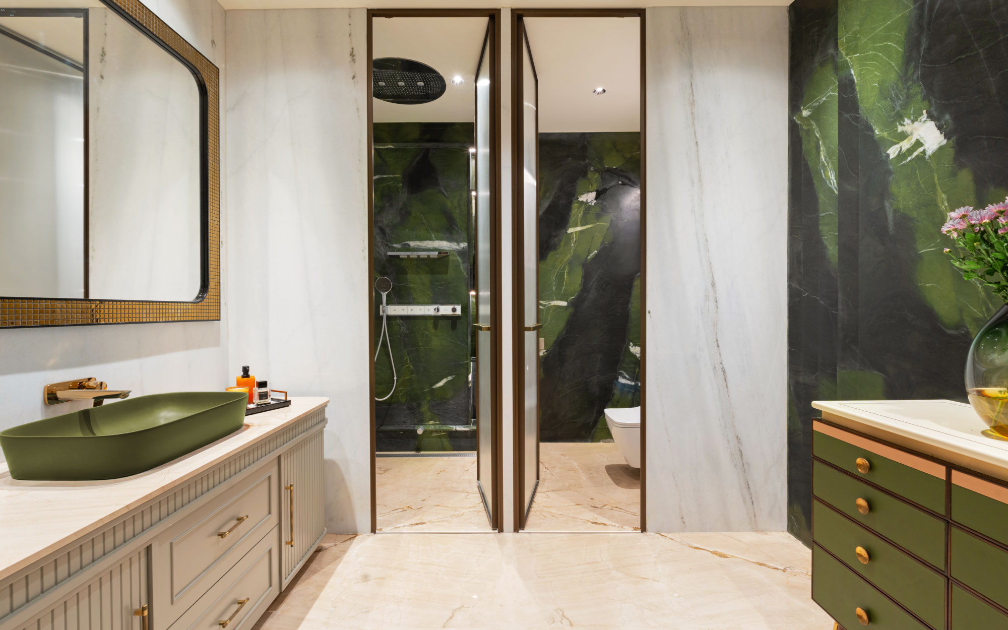 The bathroom is wrapped in striking floor-to-ceiling Brazilian Avocado Quartzite stone, its rich veining bringing depth and natural drama to the space. A statement mirror from Apartment 9 adds a touch of sculptural elegance, while vases from Armoire offer a refined, organic accent that softens the bold material palette. (Image Credits: Gitesh Gupta, Studio Bluora)
