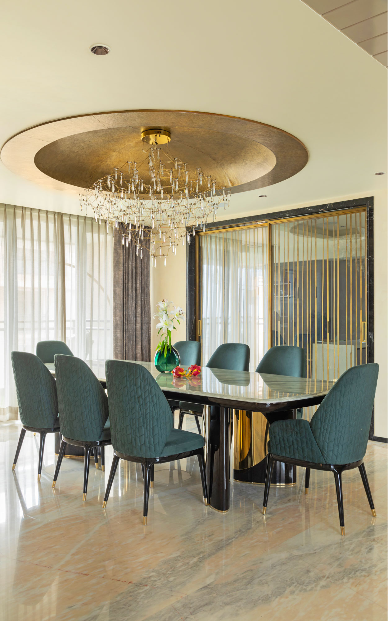 The dining area features a custom-made solid wood table, set against Michael Angelo marble flooring. Overhead, a brass dome, made with a single sheet of brass, and dangling pendants from Ledos add a warm, focused glow that ties in with the home’s understated material palette. (Image Credits: Gitesh Gupta, Studio Bluora)