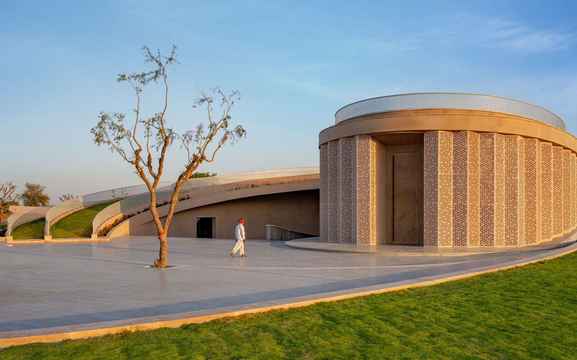 The façade, sculpted in sandstone with intricate jali screens and wrapped in an earth berm while offering climate-responsive shelter. (Image Credits: Vinay Panjwani)
