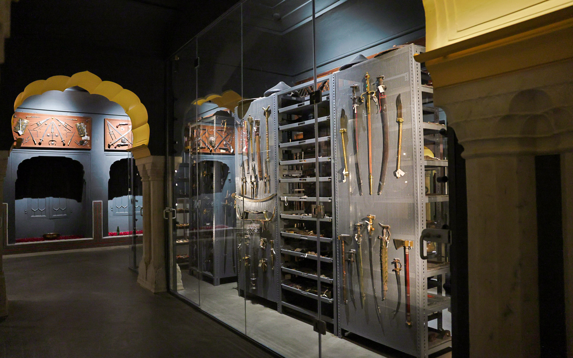 The armoury room is dimly lit, allowing the intricately incised arms to emerge in prominence, while the golden arches glow softly, framing the collection with subtle grandeur. (Image Credits: City Palace Museum)