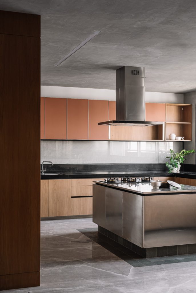 The kitchen features a stainless steel island, stain-resistant Kota flooring, dark stone countertops, terracotta surfaces and wooden cabinetry. The modular kitchen was crafted by Plezza. (Image Credit: Ishita Sitwala)