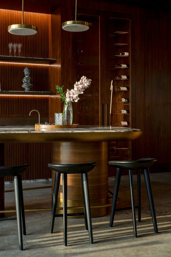 An island bar crafted from Calacatta Viola marble with walnut veneer-wrapped legs and a brass foot railing is a bespoke creation designed by Dieter Vander Velpen Architects. The bar stools are a BassamFellows design. (Image Credit: Patricia Goijens)