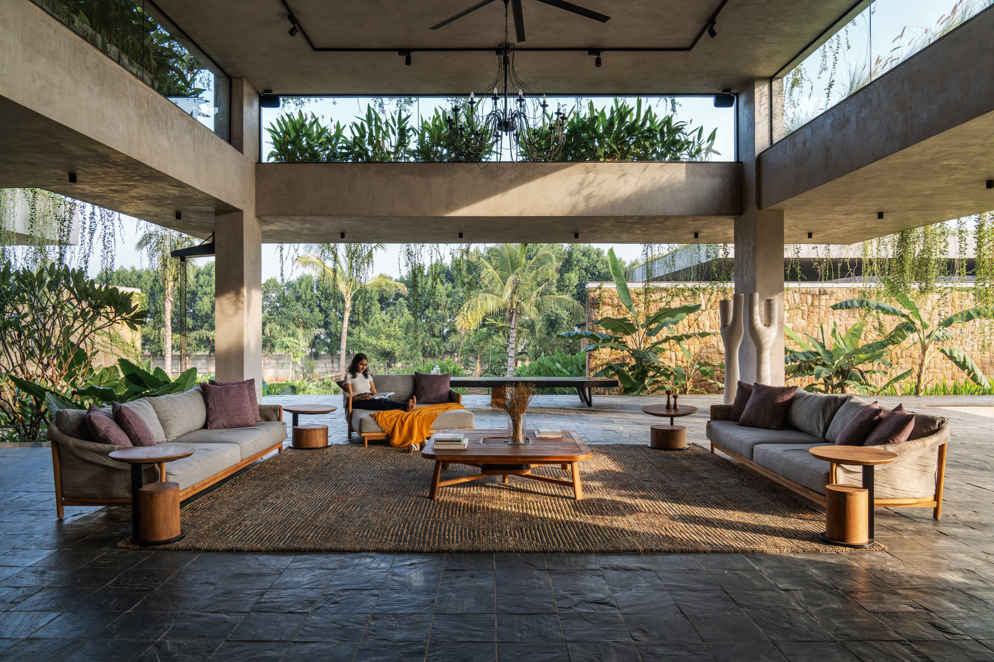 The covered, open verandah is lined with a massive jute carpet executed by The Rug Story. Furniture in an earthy palette by Dbodhi & Otazen imitates the hues of the natural backdrop.  (Image Credits: Shamanth Patil)
