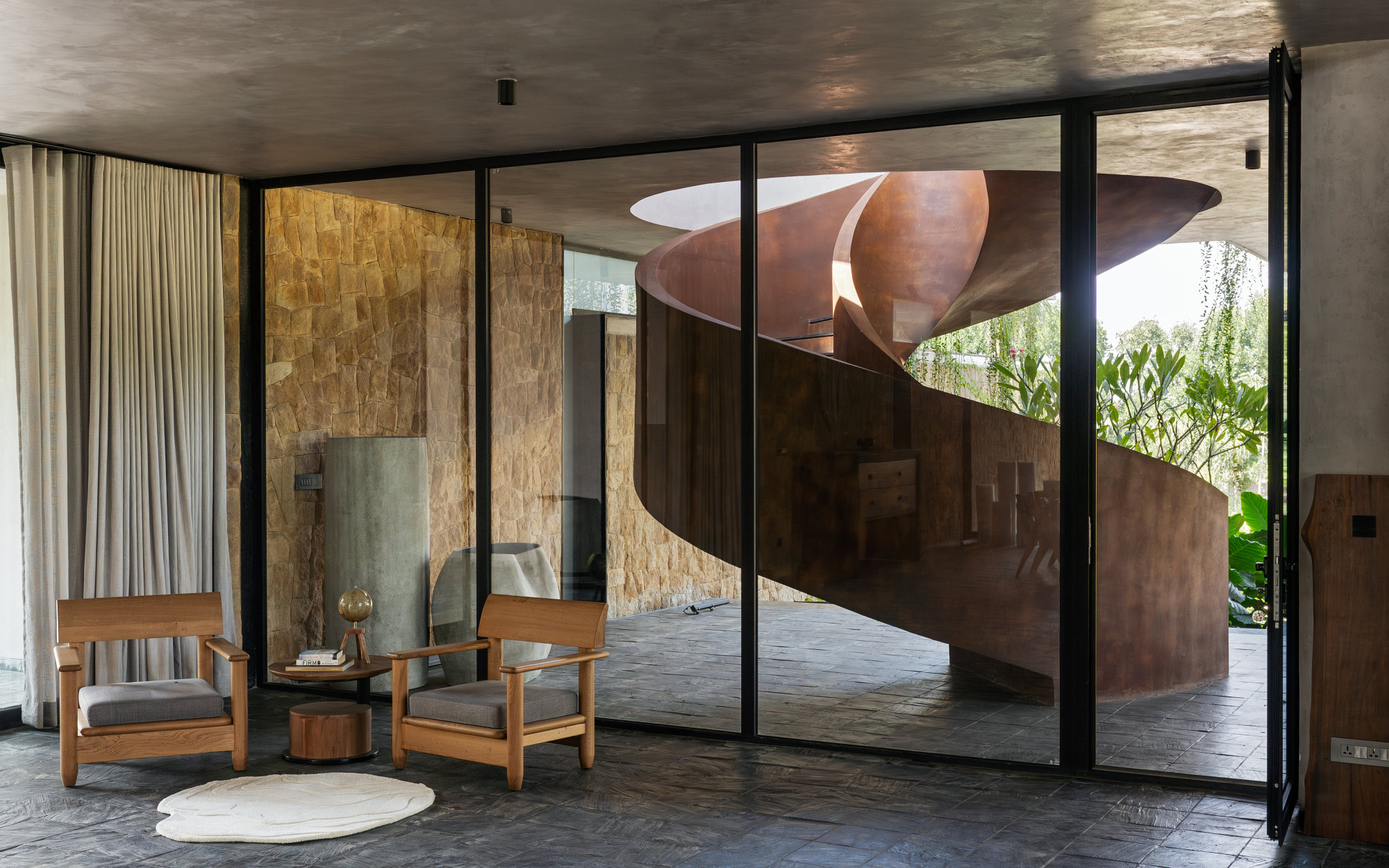 An indoor-outdoor seating space is punctuated by glazing systems from Pinkmondo. The spiral staircase commands attention, bringing forth an element of liquid metal.  (Image Credits: Shamanth Patil)
