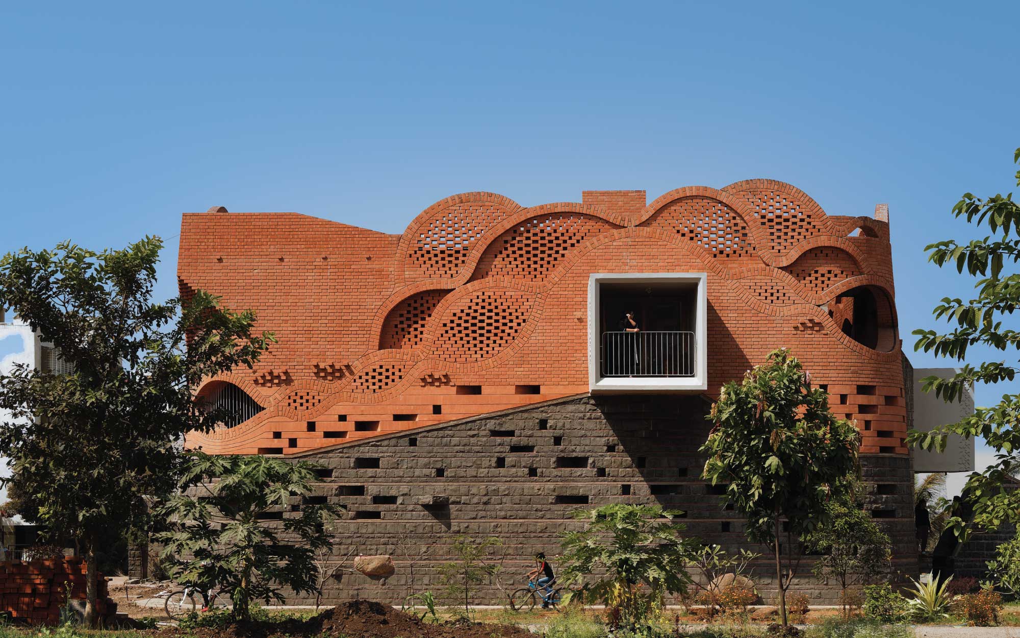 The façade transitions from a heavy stone base to soft, scalloped brickwork above. (Image Credits: Hemant Patil)