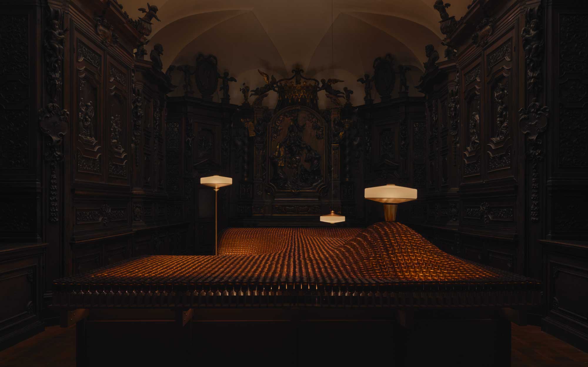 A glowing topography of amber glass unfurls beneath the Aposē lamps, where Aesop stages light as both material and mood within the historic confines of Santa Maria del Carmine. (Image Credits: Aesop)
