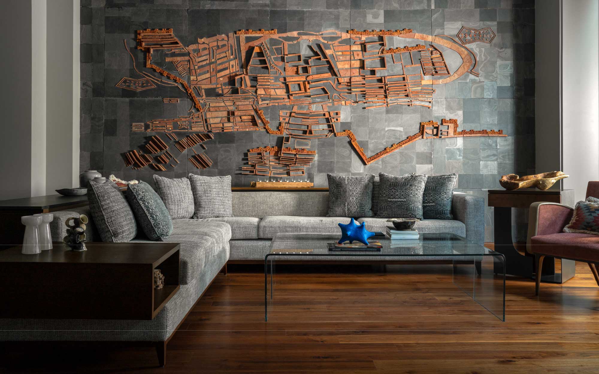 An earthy colour palette with browns and greys, this family lounge hosts an L-shaped sofa set, wooden flooring with a large-scale mural composed of brick and slate. (Image Credits: Avesh Gaur)
