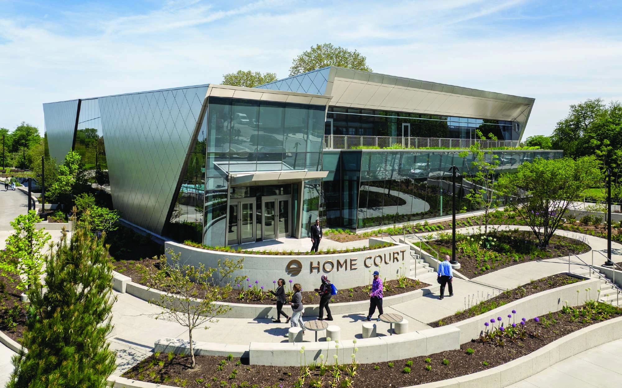 The Home Court features a bold, diamond-patterned metallic exterior intersected by sweeping, angular glass walls revealing warm interiors. (Image Credit: Angie McMonigal)